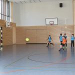 Kinder spielen Fußball in einer Turnhalle.