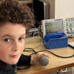 Junge mit Mikrofon vor Oszilloskop im Labor