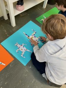 Kindergartenkinder basteln bunte Froschbilder auf Papier.
