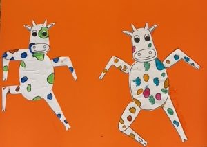 Bunte Pappkühe tanzen auf orangefarbenem Hintergrund